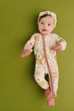 Baby in a patterned onesie and headband against a green background