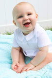 Baby wearing a white romper, sitting on a blue blanket with a white background