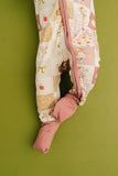 Baby in a quilted outfit with pink foot covers against a green background