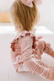 Child wearing a pink velvet long sleeve romper with shoulder ruffles on a white background