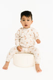Child wearing a white outfit with a mallard pattern, sitting on a white stool against a white background.