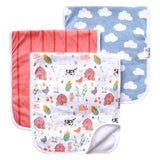 Three burp cloths with rounded corners are arranged overlapping on a white background. The front cloth is white with a colorful farm illustration pattern including barns, cows, chickens, and plants.