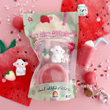 A toy milkshake set in a clear bag with a pastel green label reading 'Moo Moo Milkshake' and 'Play with Purpose.' The package contains a pink drink cup, a small white cow figure, and a strawberry-themed accessory, arranged on a pink surface with strawberry and candy props.