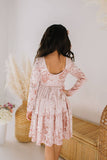 girl wearing a pink velvet dress with long sleeves and a scooped back in a minimalistic setting.
