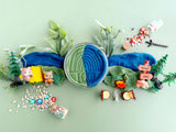 Decorative setup with a circular play dough container, small figurines, and plants on a light green background