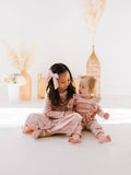Two children in matching pink velvet outfits sitting on a white floor with decorative elements in the background.