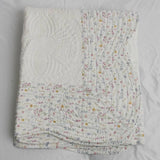 White quilted blanket with floral patterned trim on a plain background