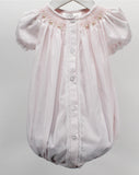 A light pink baby romper with short puff sleeves, a button-down front, lace trim, and delicate floral embroidery and smocking around the neckline, hanging on a white hanger against a neutral gray background.
