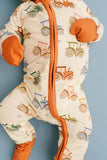 A baby footed sleeper with an orange zipper, orange cuffs and foot, and a cream background printed with colorful tractors, shown against a solid blue background.