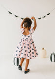 Child wearing a pink dress with black cat pattern, standing in front of Halloween decorations.