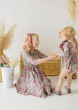 Two children in matching floral long sleeve outfits standing in a room with decorative elements.