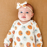 Baby wearing a white knotted gown with orange pumpkin patterns on a brown background