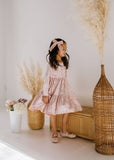 Young girl in a pink velvet dress standing in a room with decorative elements.