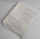 white quilted blanket with floral patterned trim on a plain background