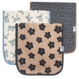 Three burp cloths. The front cloth is beige with black flower patterns, the middle cloth is cream with light blue bows, and the back cloth is dark gray with gold polka dots.