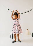 Child wearing a pink dress with black cat pattern, standing in front of Halloween decorations.