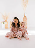 Two children in matching pink velvet outfits sitting on a white surface with a neutral background.