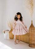 Young girl in a long sleeve pink velvet dress standing in a room with decorative elements.