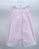 A light pink sleeveless baby dress with white lace trim on the collar and hem and buttons down the back, hanging on a white hanger against a light gray background.