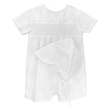 boys white shorts romper with collar and smocking detail across the chest. Matching white bonnet laying on top of romper. Romper is on a white background. 